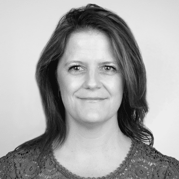 Black and white portrait of a smiling middle-aged woman with shoulder-length hair, wearing a lace-detailed top, against a plain background.
